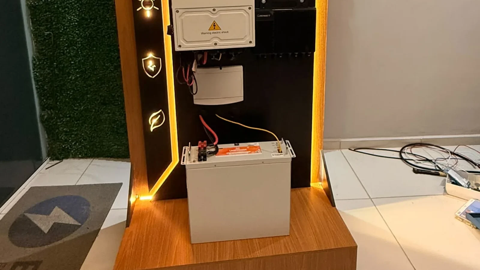 Kit de demonstração com inversor híbrido e bateria de armazenamento exibido em estande da Eletroserv, com tela mostrando instalação solar