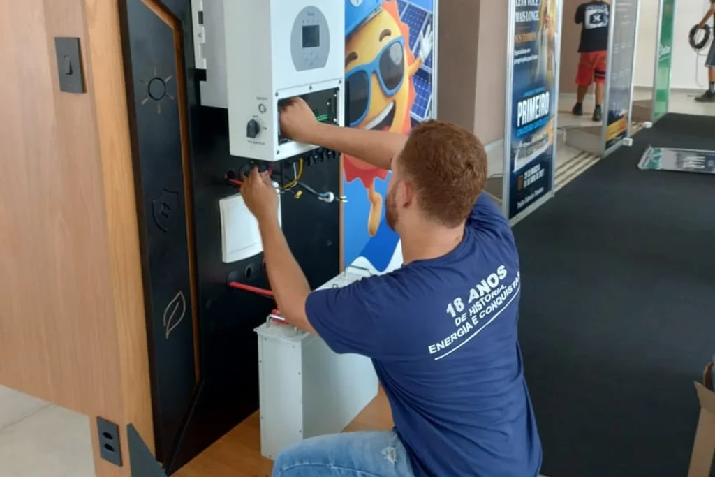 Técnico da Eletroserv, uniformizado, ajustando componentes elétricos de kit demonstrativo durante evento