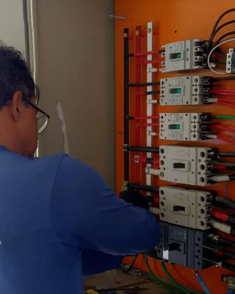 Técnico da Eletroserv realizando manutenção em quadro elétrico industrial com múltiplos disjuntores e cabeamento organizado