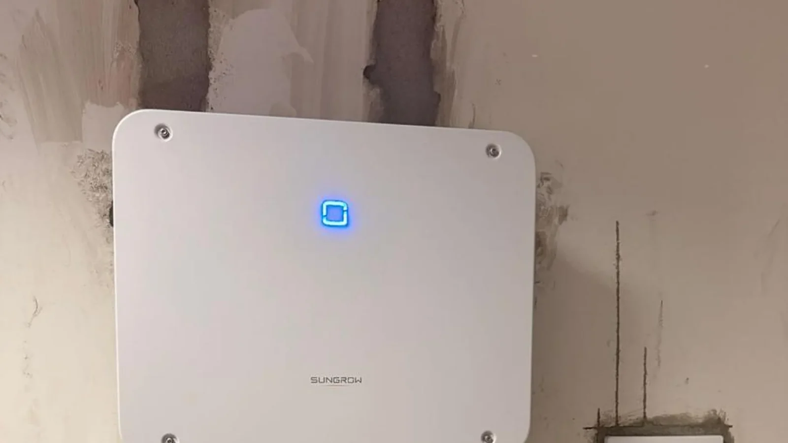 Inversor solar de marca Sungrow instalado em parede, com caixas de conexão e cabeamento elétrico organizado