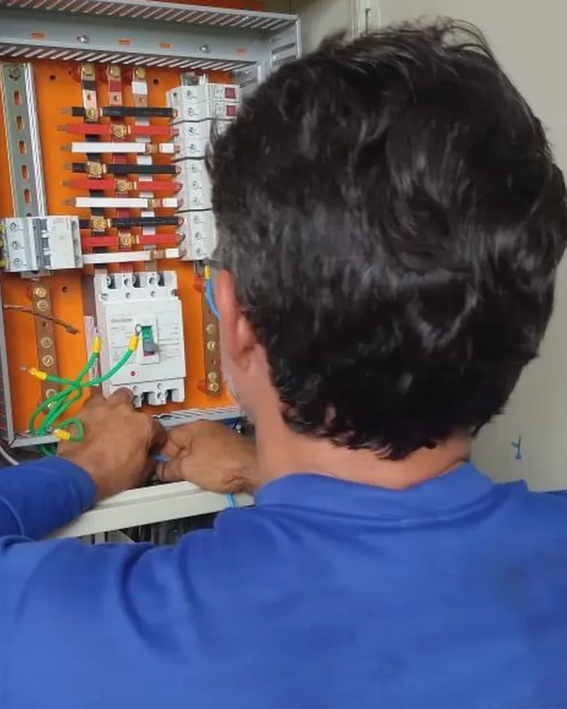 Eletricista da Eletroserv trabalhando em quadro de distribuição elétrica aberto, com disjuntores e barramentos visíveis