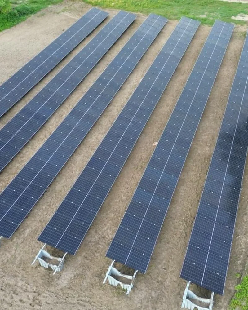 Vista aérea de usina solar com fileiras de painéis fotovoltaicos instalados sobre estrutura em solo, rodeada por vegetação