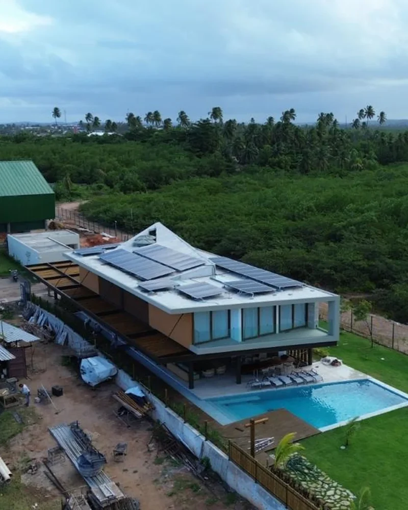 Vista aérea de residência moderna com piscina e painéis solares no telhado, cercada por vegetação nativa