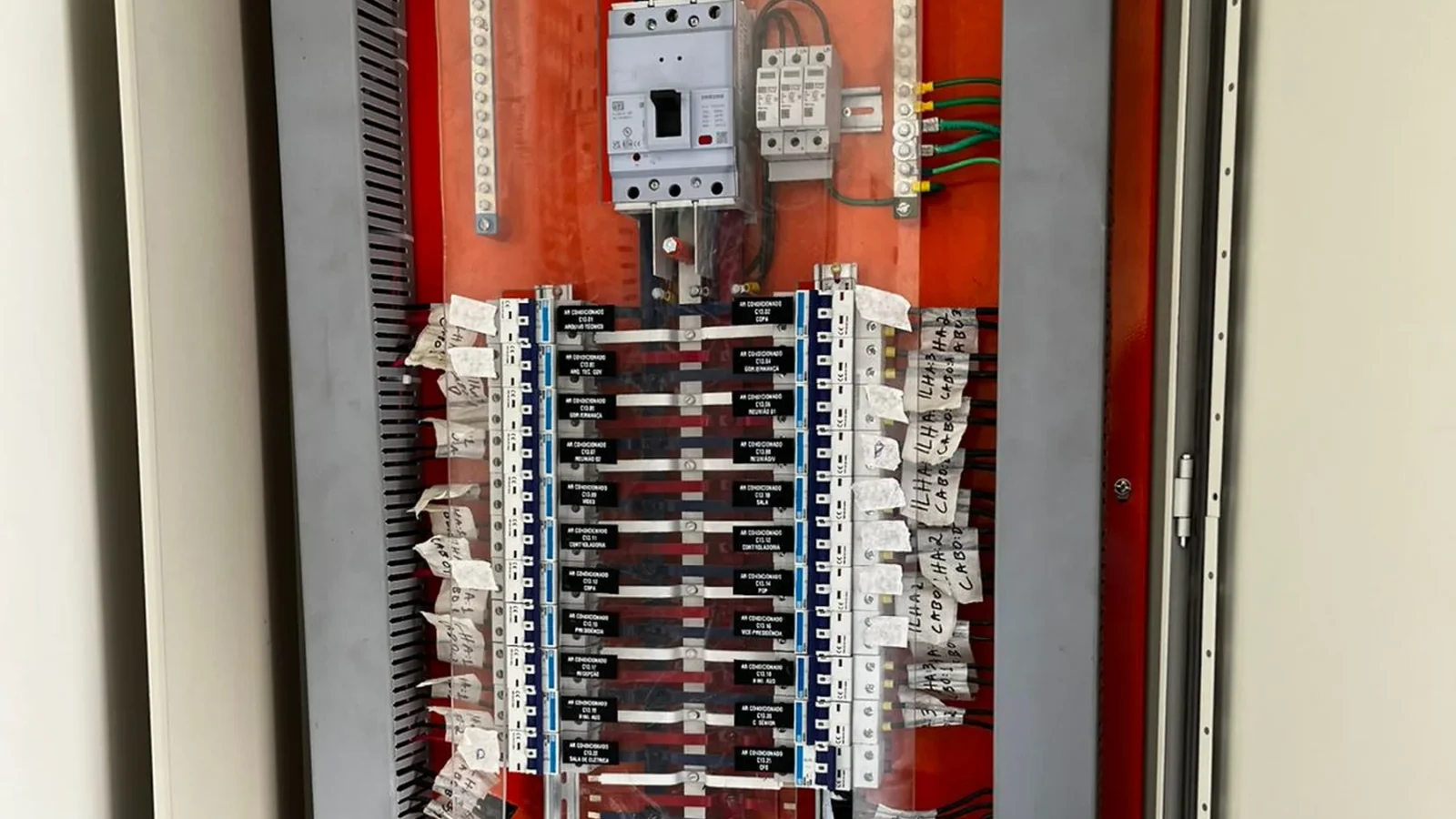 Quadro de distribuição elétrica aberto com múltiplos disjuntores etiquetados, barramento vermelho e fiação organizada.