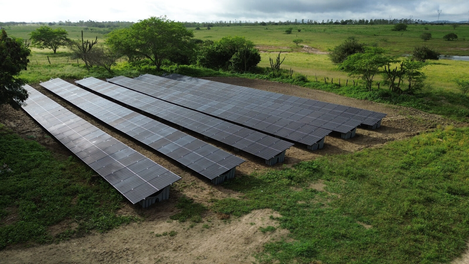 Vista aérea de usina fotovoltaica com painéis solares instalados sobre estrutura em solo, cercada por vegetação verde
