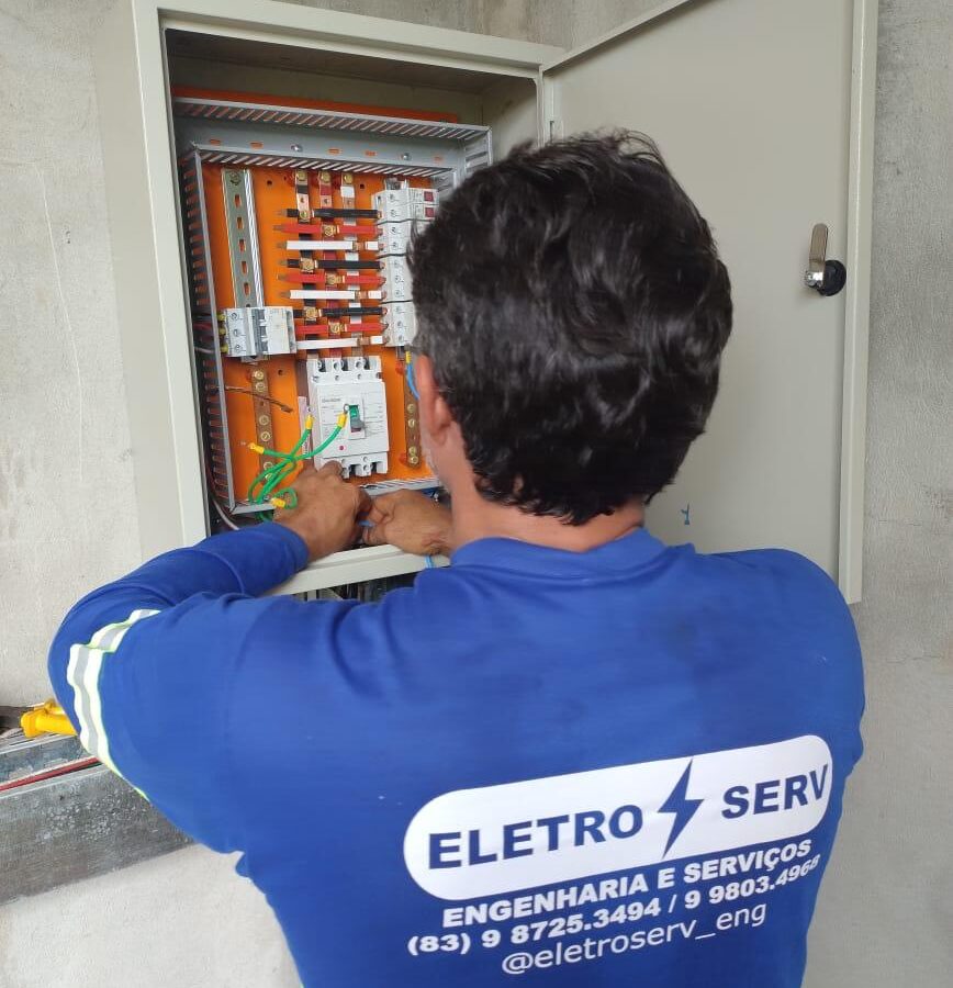 Eletricista da Eletroserv trabalhando em quadro de distribuição elétrica aberto, com disjuntores e barramentos visíveis