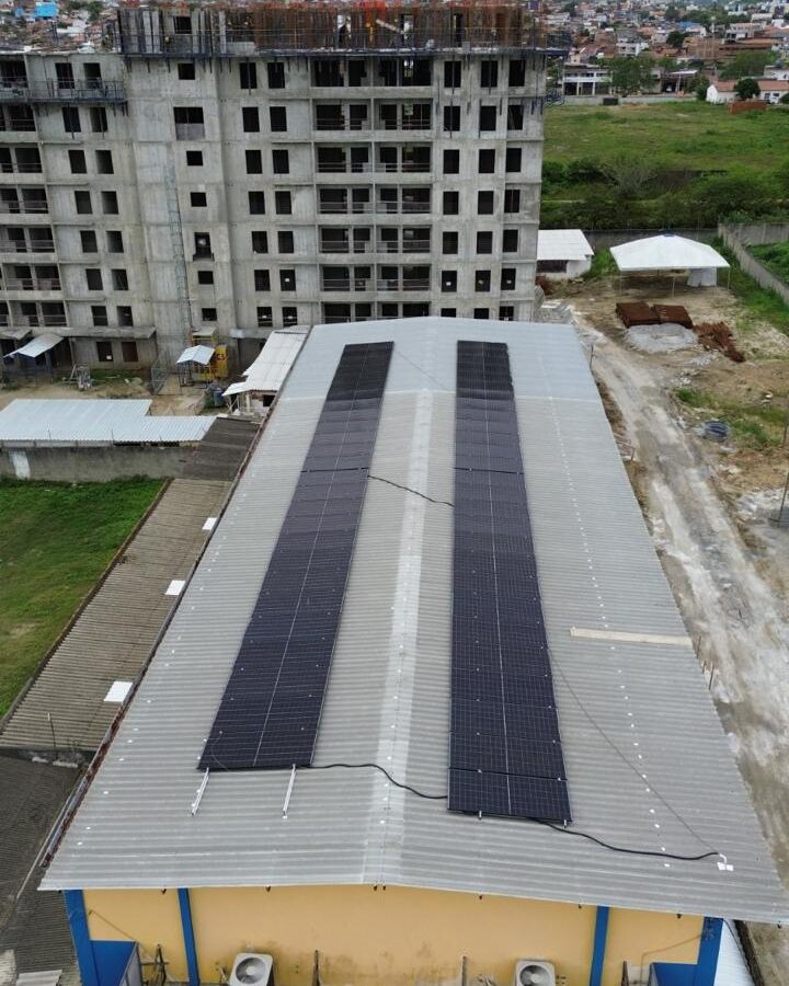 Vista aérea de telhado comercial com painéis solares instalados, prédio em construção ao fundo em área urbana
